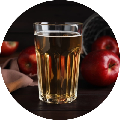 A glass of apple juice is placed on a dark wooden table with red apples.