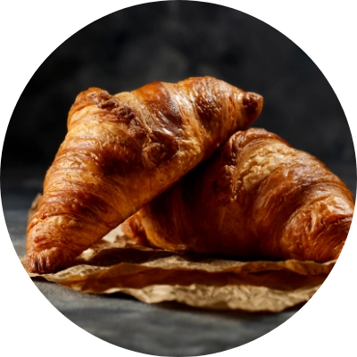 Two golden brown croissants sit on crumpled brown parchment paper against a dark background.