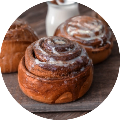 Three cinnamon rolls, crafted by Preligen Artisan Bakery, rest on a dark wooden surface, with a bottle of milk in the background.