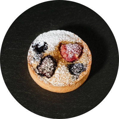 A small tart filled with berries, lightly dusted with powdered sugar.