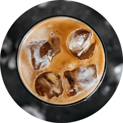 A top view of an iced coffee with milk in a glass, brimming with several ice cubes.