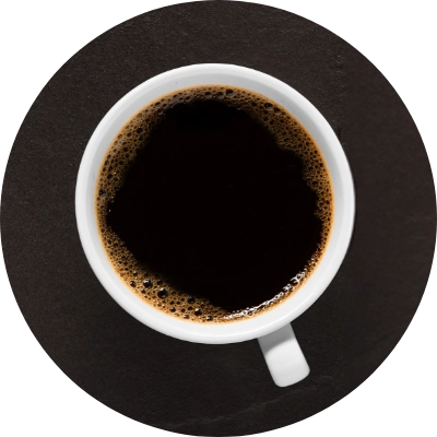 A top view of a white cup filled with black coffee, placed on a dark surface.