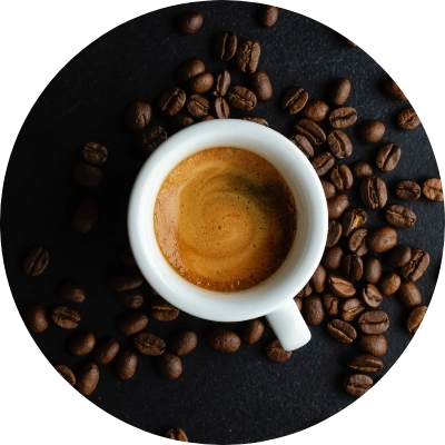 A cup of espresso from Preligen Artisan Bakery surrounded by scattered coffee beans on a dark surface.