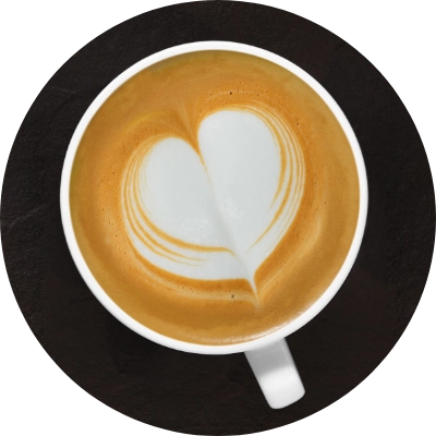 A cup of coffee with a heart-shaped pattern in the foam, viewed from above, placed on a dark surface.