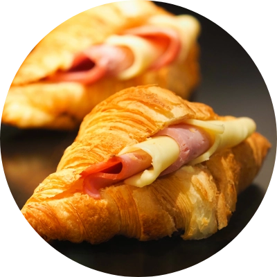 Two buttery croissants filled with slices of ham and cheese, displayed on a dark surface.