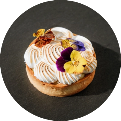 A lemon curd with Swiss Meringue tart from our San Jose bakery, garnished with purple, yellow, and orange edible flowers.