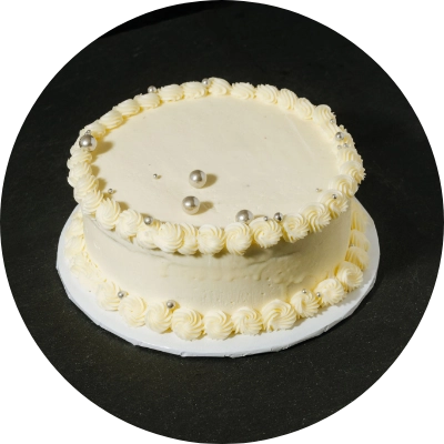 A round white frosted cake with a decorative rosette border and silver edible beads on top.