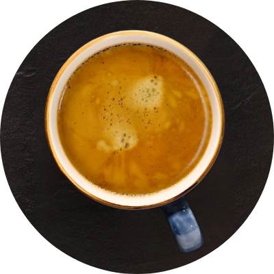 A ceramic mug filled with frothy coffee, viewed from above, placed on a dark surface.