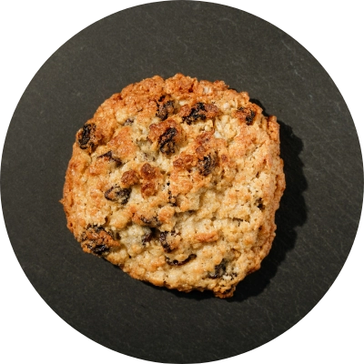 A crunchy oatmeal raisin cookie with a golden-brown texture rests on a dark surface.