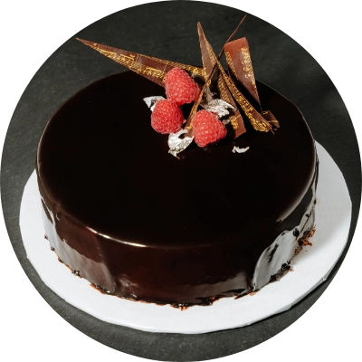 A round raspberry mousse chocolate cake with a glossy finish, garnished with raspberries, pieces of chocolate, and edible silver flakes, placed on a white plate.