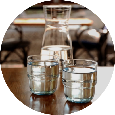 A carafe filled with water and two glasses of water are placed on a wooden table.